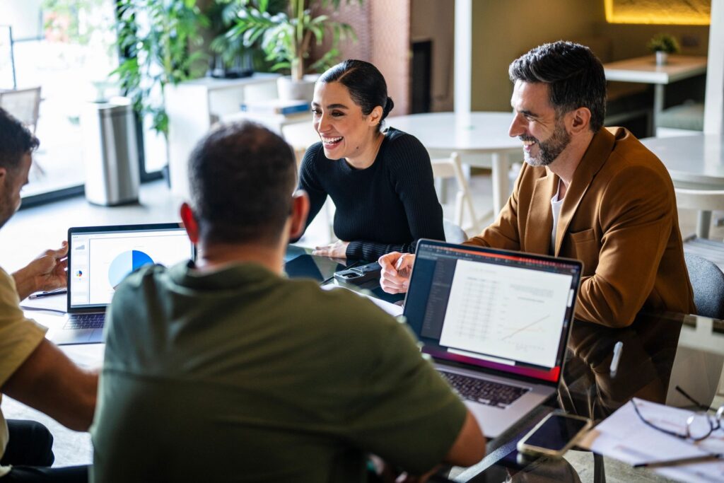 Group of cheerful multiracial business colleagues in meeting, discussing and smiling with laptops